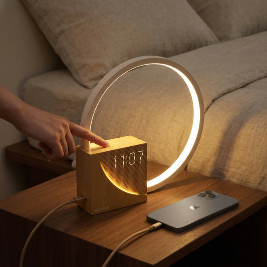 Modern wooden digital alarm clock with a circular ring light and smartphone on a bedside table