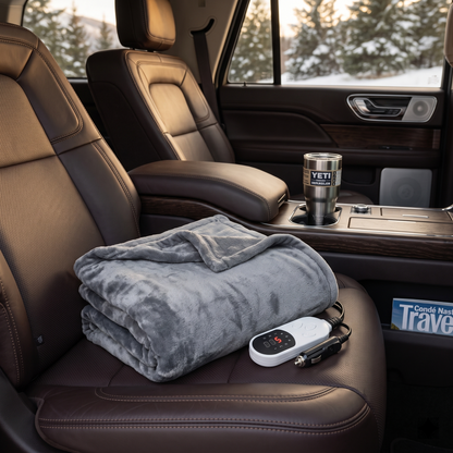 Grey electric heated blanket with digital controller on a brown leather car seat.