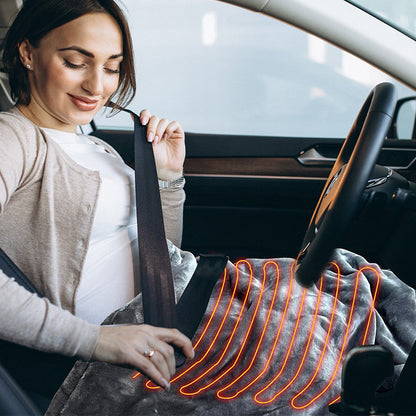 A pregnant woman sitting in a car seat using a heated grey blanket.